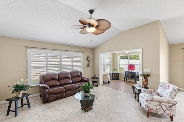 living area featuring lofted ceiling, baseboards, light tile patterned floors, a textured ceiling, and ceiling fan