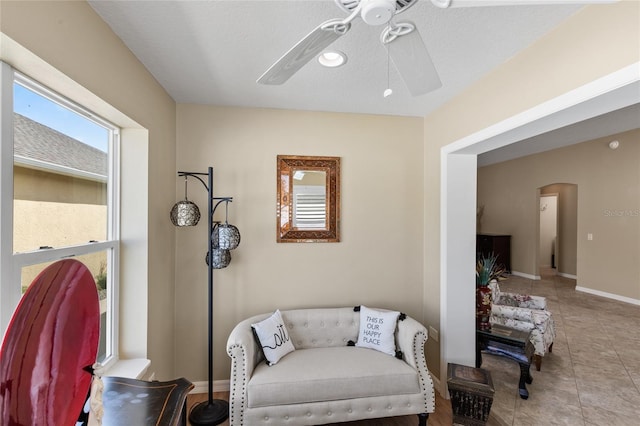 sitting room with arched walkways, ceiling fan, baseboards, and tile patterned flooring