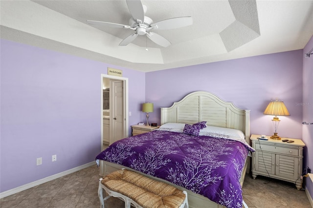 tiled bedroom with a tray ceiling, baseboards, connected bathroom, and ceiling fan