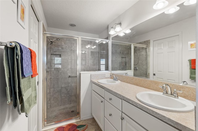 bathroom with a stall shower, double vanity, a sink, and a textured ceiling