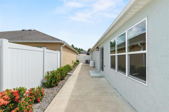 view of side of property with a patio, a shingled roof, stucco siding, and fence