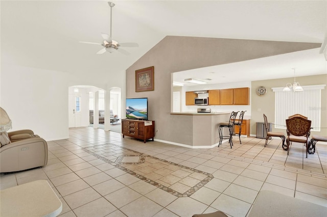 living area featuring light tile patterned floors, ceiling fan with notable chandelier, arched walkways, and baseboards