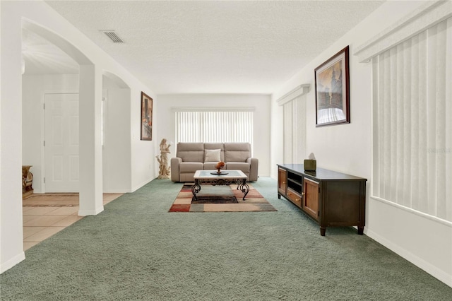 living room with visible vents, a textured ceiling, arched walkways, carpet flooring, and tile patterned flooring