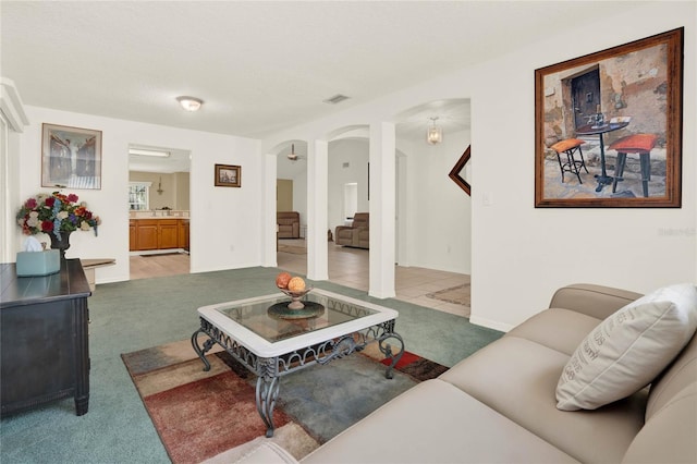 carpeted living room with arched walkways, visible vents, and baseboards