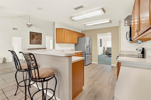 kitchen with a peninsula, appliances with stainless steel finishes, a breakfast bar area, light countertops, and decorative backsplash