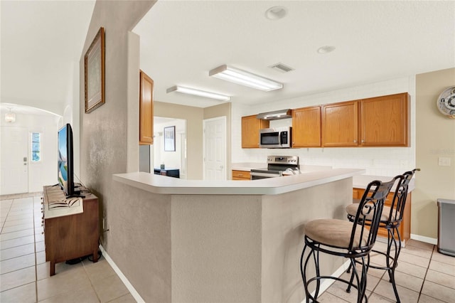 kitchen with visible vents, a breakfast bar, arched walkways, appliances with stainless steel finishes, and light tile patterned floors