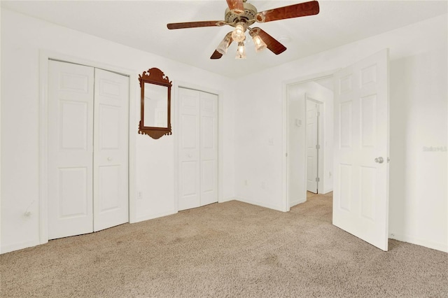 unfurnished bedroom with two closets, carpet, and a ceiling fan