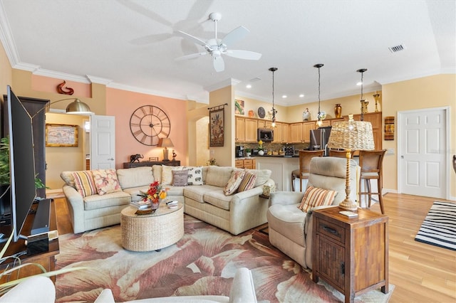 living room with light wood-type flooring, ornamental molding, and ceiling fan