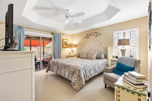 carpeted bedroom featuring a tray ceiling, access to outside, and ceiling fan