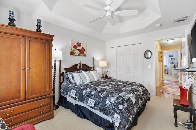 carpeted bedroom featuring a textured ceiling, ceiling fan, a closet, and a tray ceiling