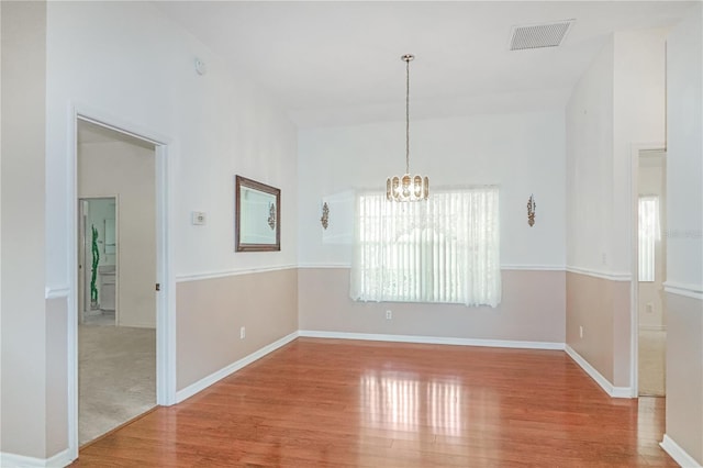 empty room featuring visible vents, baseboards, an inviting chandelier, and wood finished floors