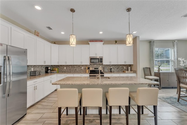 kitchen featuring white cabinets, appliances with stainless steel finishes, light stone countertops, and a center island with sink