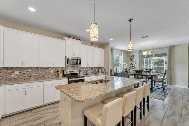 kitchen featuring a center island with sink, pendant lighting, appliances with stainless steel finishes, and white cabinets