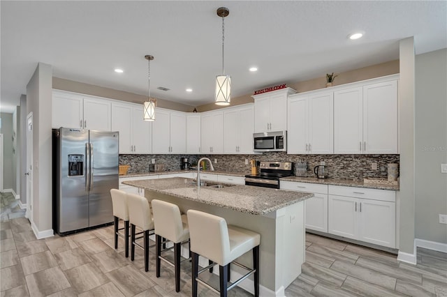 kitchen featuring appliances with stainless steel finishes, white cabinetry, sink, a kitchen bar, and a kitchen island with sink