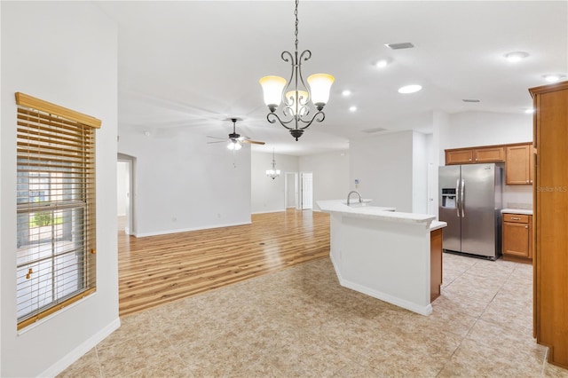 kitchen featuring a kitchen island with sink, ceiling fan with notable chandelier, stainless steel fridge, vaulted ceiling, and light hardwood / wood-style floors