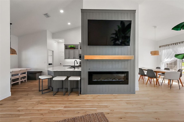 kitchen with kitchen peninsula, a fireplace, light wood-type flooring, and vaulted ceiling