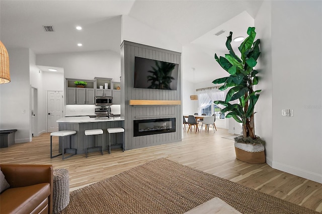 living room with light wood-type flooring, a fireplace, sink, and vaulted ceiling