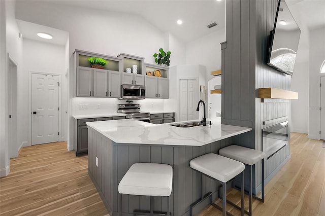 kitchen featuring high vaulted ceiling, gray cabinetry, appliances with stainless steel finishes, and light hardwood / wood-style flooring