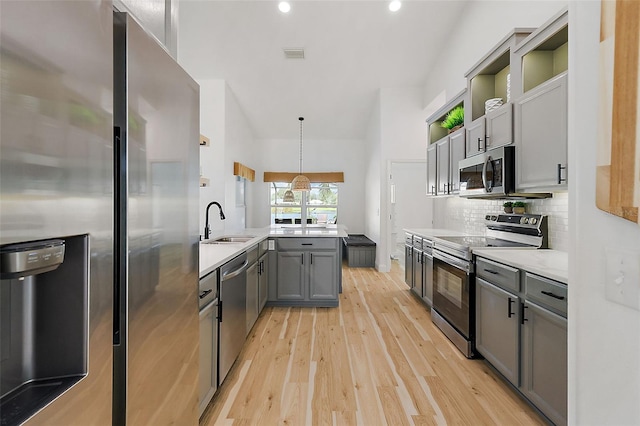 kitchen featuring stainless steel appliances, light hardwood / wood-style floors, hanging light fixtures, sink, and gray cabinetry