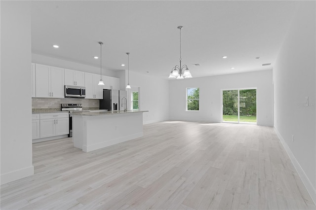 kitchen with a center island with sink, stainless steel appliances, light stone counters, and white cabinetry