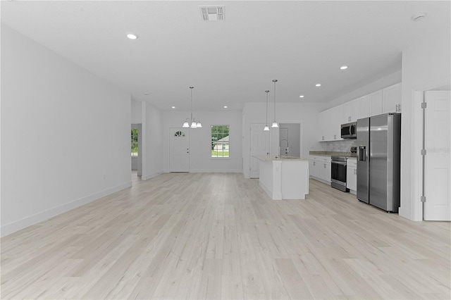 kitchen featuring white cabinets, an inviting chandelier, light hardwood / wood-style flooring, stainless steel appliances, and a center island with sink