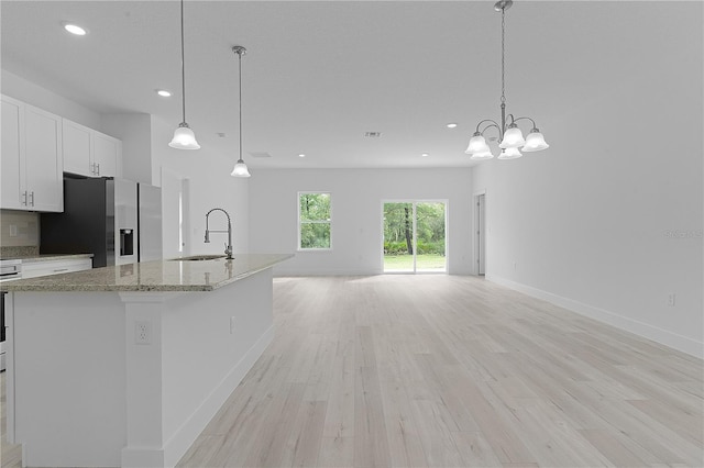 kitchen featuring light stone counters, light hardwood / wood-style floors, sink, pendant lighting, and stainless steel fridge with ice dispenser