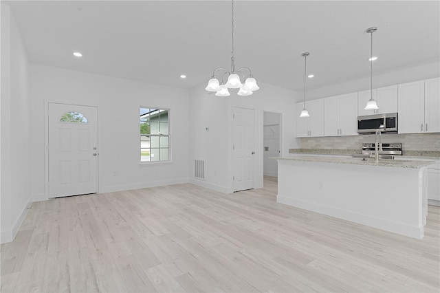 kitchen featuring a kitchen island with sink, white cabinetry, light stone countertops, appliances with stainless steel finishes, and light hardwood / wood-style floors