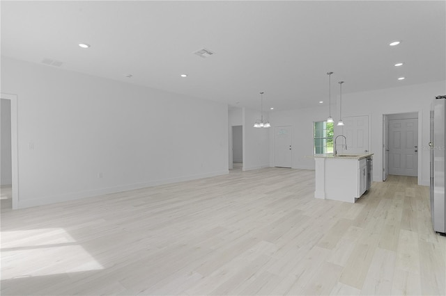 unfurnished living room with light hardwood / wood-style flooring, an inviting chandelier, and sink