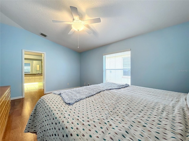 bedroom with a textured ceiling, hardwood / wood-style floors, connected bathroom, lofted ceiling, and ceiling fan