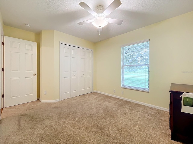 unfurnished bedroom with a textured ceiling, light colored carpet, ceiling fan, and a closet