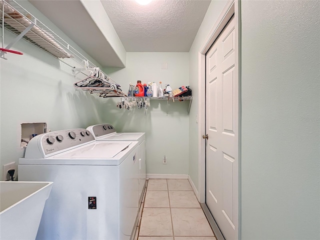 clothes washing area with light tile patterned floors, a textured ceiling, washer and clothes dryer, and sink