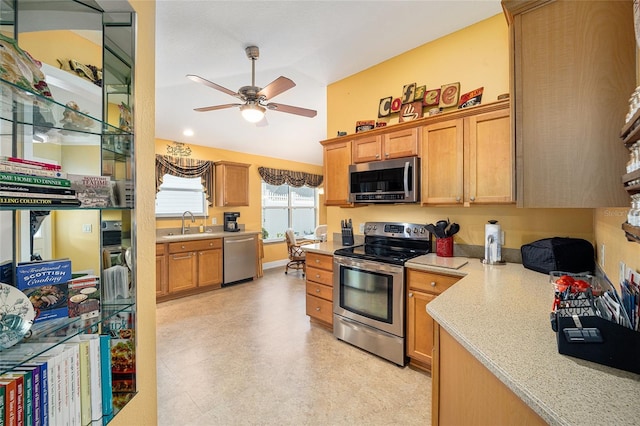 kitchen featuring appliances with stainless steel finishes, built in desk, light stone counters, ceiling fan, and sink