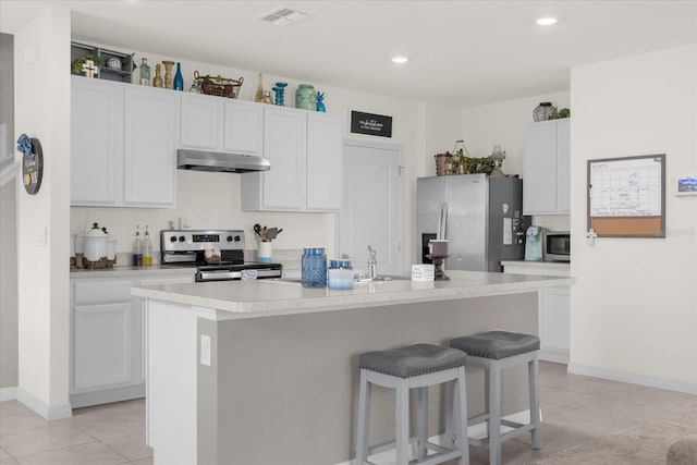 kitchen featuring a kitchen island with sink, a kitchen bar, light tile patterned floors, stainless steel appliances, and white cabinets