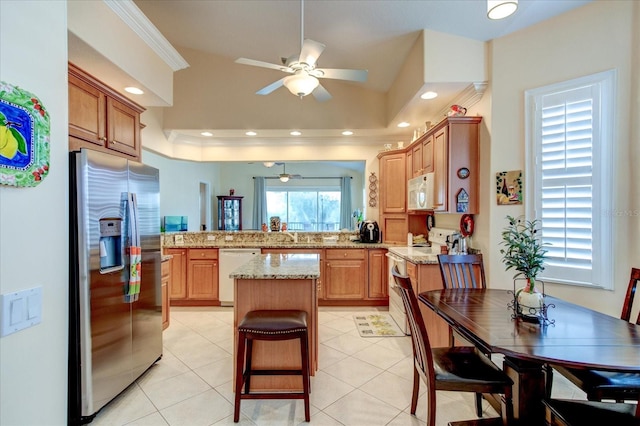 kitchen featuring light tile patterned floors, a center island, light stone countertops, stainless steel appliances, and ceiling fan