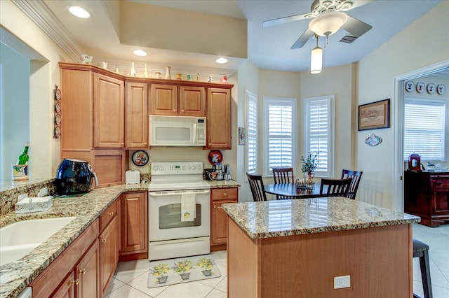 kitchen with light tile patterned floors, white appliances, light stone countertops, ceiling fan, and a kitchen bar