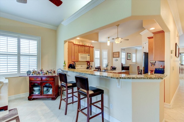 kitchen featuring ornamental molding, light tile patterned floors, kitchen peninsula, ceiling fan, and a breakfast bar area