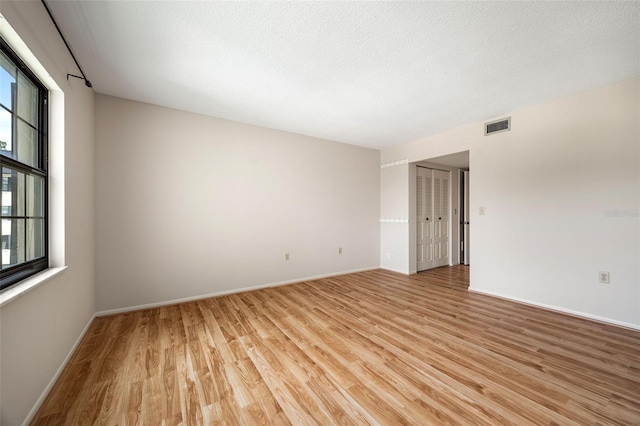 empty room with a textured ceiling and light hardwood / wood-style floors