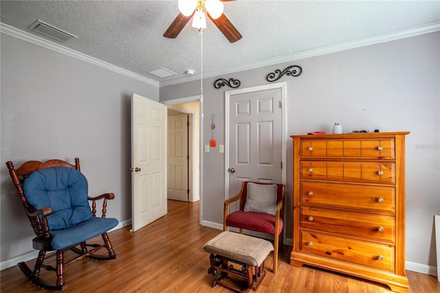 living area with a textured ceiling, crown molding, ceiling fan, and light wood-type flooring