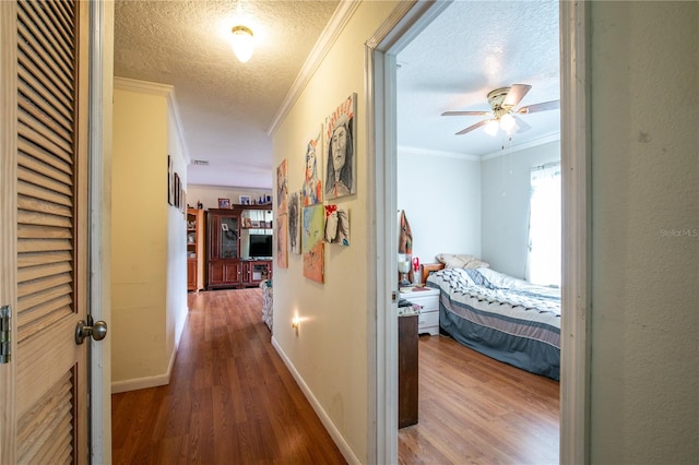 hall with a textured ceiling, ornamental molding, and hardwood / wood-style floors