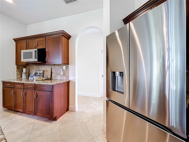 kitchen featuring light stone countertops, appliances with stainless steel finishes, light tile patterned floors, and decorative backsplash