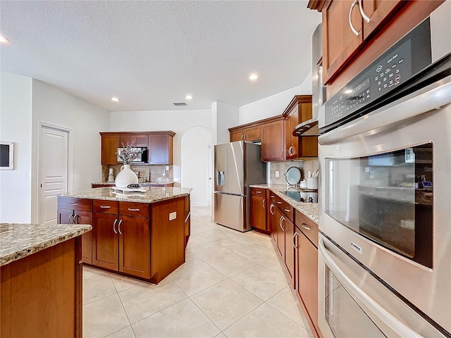 kitchen with light tile patterned flooring, a textured ceiling, backsplash, appliances with stainless steel finishes, and light stone countertops