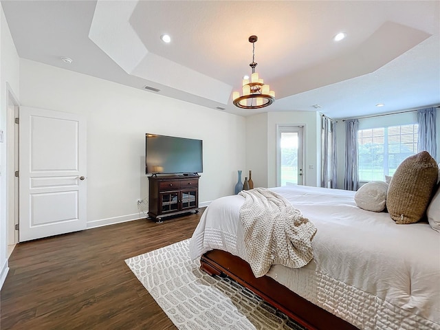 bedroom featuring an inviting chandelier, a tray ceiling, and dark wood-type flooring