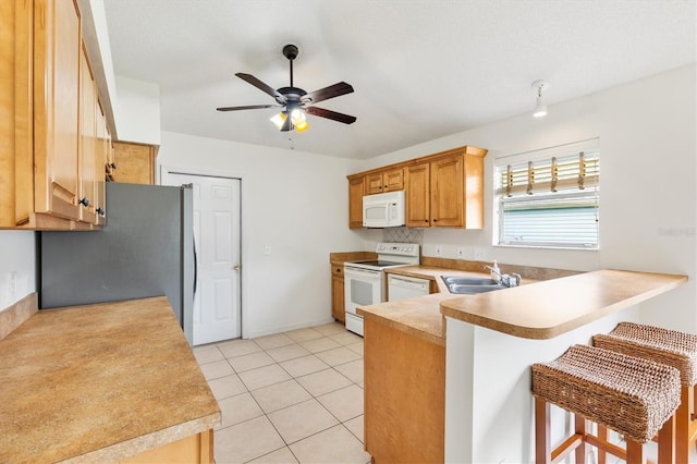 kitchen with ceiling fan, sink, kitchen peninsula, white appliances, and a kitchen breakfast bar