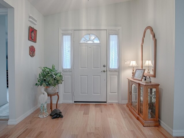 entrance foyer featuring lofted ceiling, light hardwood / wood-style flooring, and a textured ceiling