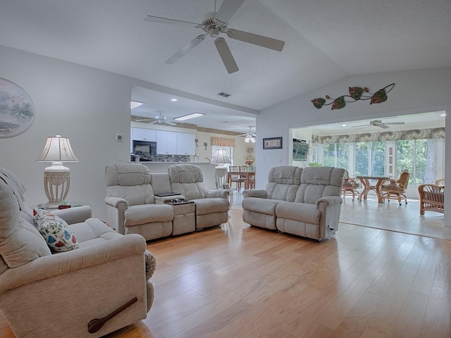 living room with lofted ceiling, ceiling fan, a textured ceiling, and light hardwood / wood-style floors