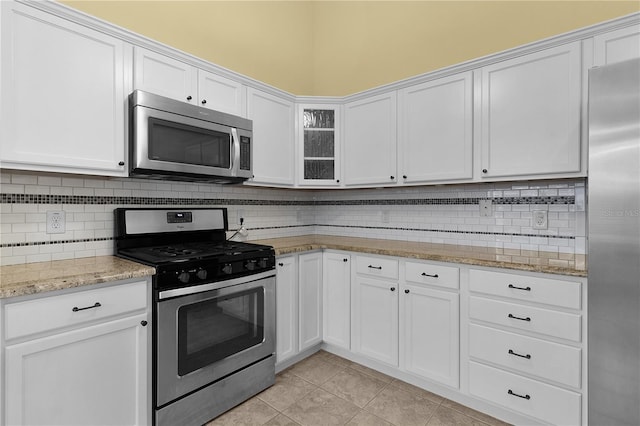 kitchen with tasteful backsplash, white cabinets, stainless steel appliances, and light tile patterned floors