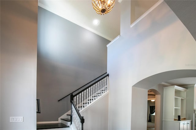 stairway with crown molding, a towering ceiling, and an inviting chandelier