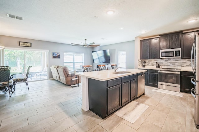 kitchen with a kitchen island with sink, sink, appliances with stainless steel finishes, dark brown cabinetry, and ceiling fan