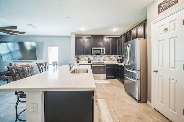 kitchen featuring a kitchen island with sink, appliances with stainless steel finishes, sink, and a kitchen breakfast bar