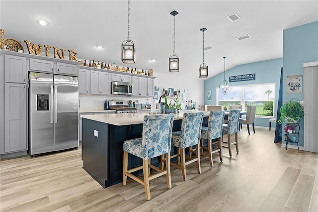 kitchen with appliances with stainless steel finishes, lofted ceiling, decorative light fixtures, a kitchen island with sink, and gray cabinetry